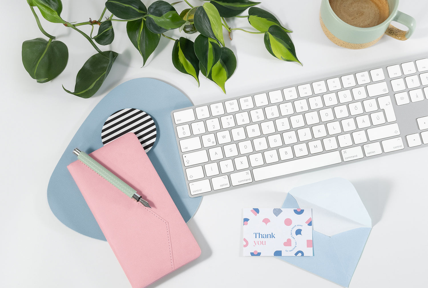 Portamira contact page illustration: Desk setup with keyboard, pink notebook, thank you card, pen, plant and coffee and on a white surface.