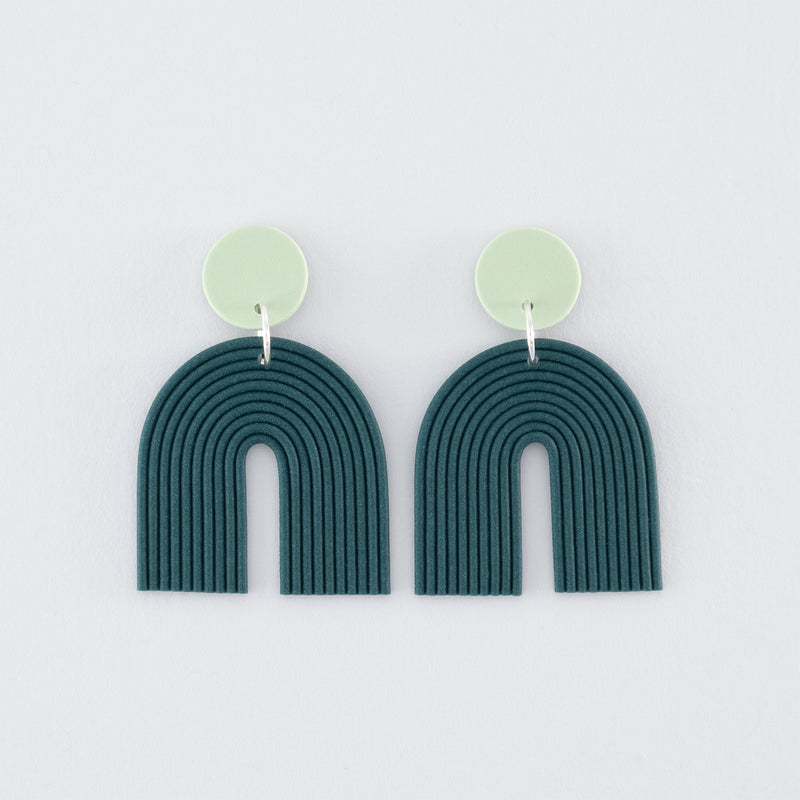 Folium N°2 handmade dangle earrings – delicate, boho, nature-inspired, arch-shaped earrings in smokey teal and pale green with 925 sterling silver findings on a light grey background.