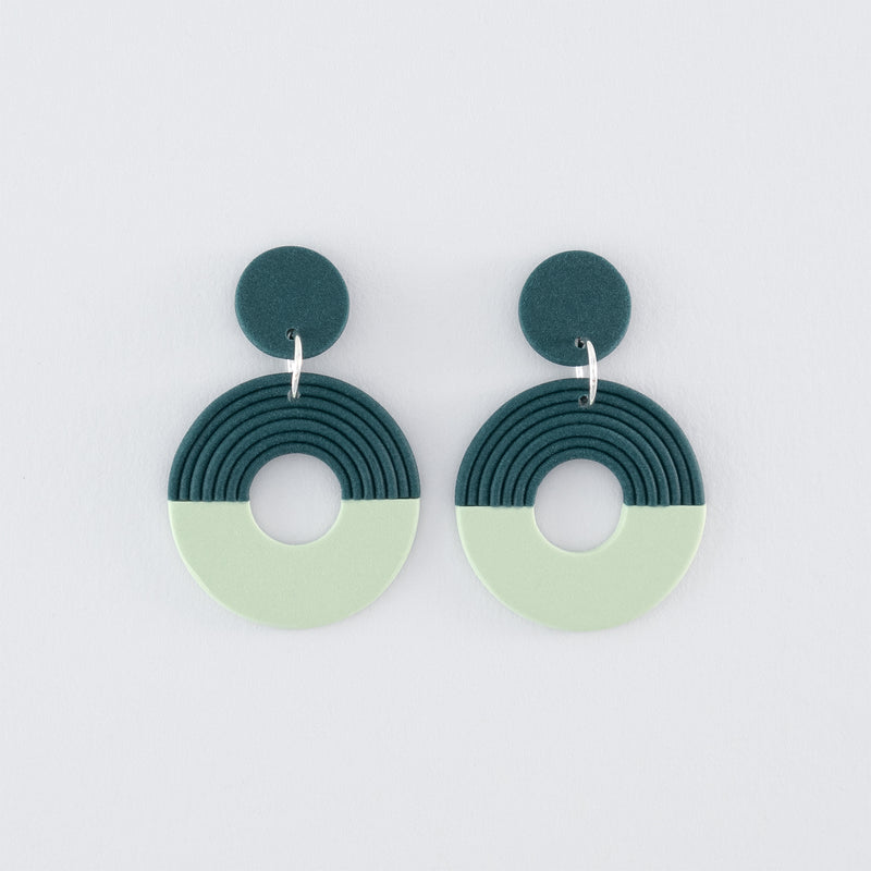 A pair of Folium N°4 handmade dangle earrings – delicate, round, nature-inspired earrings in smokey teal and pale green with 925 sterling silver findings on a light grey background.