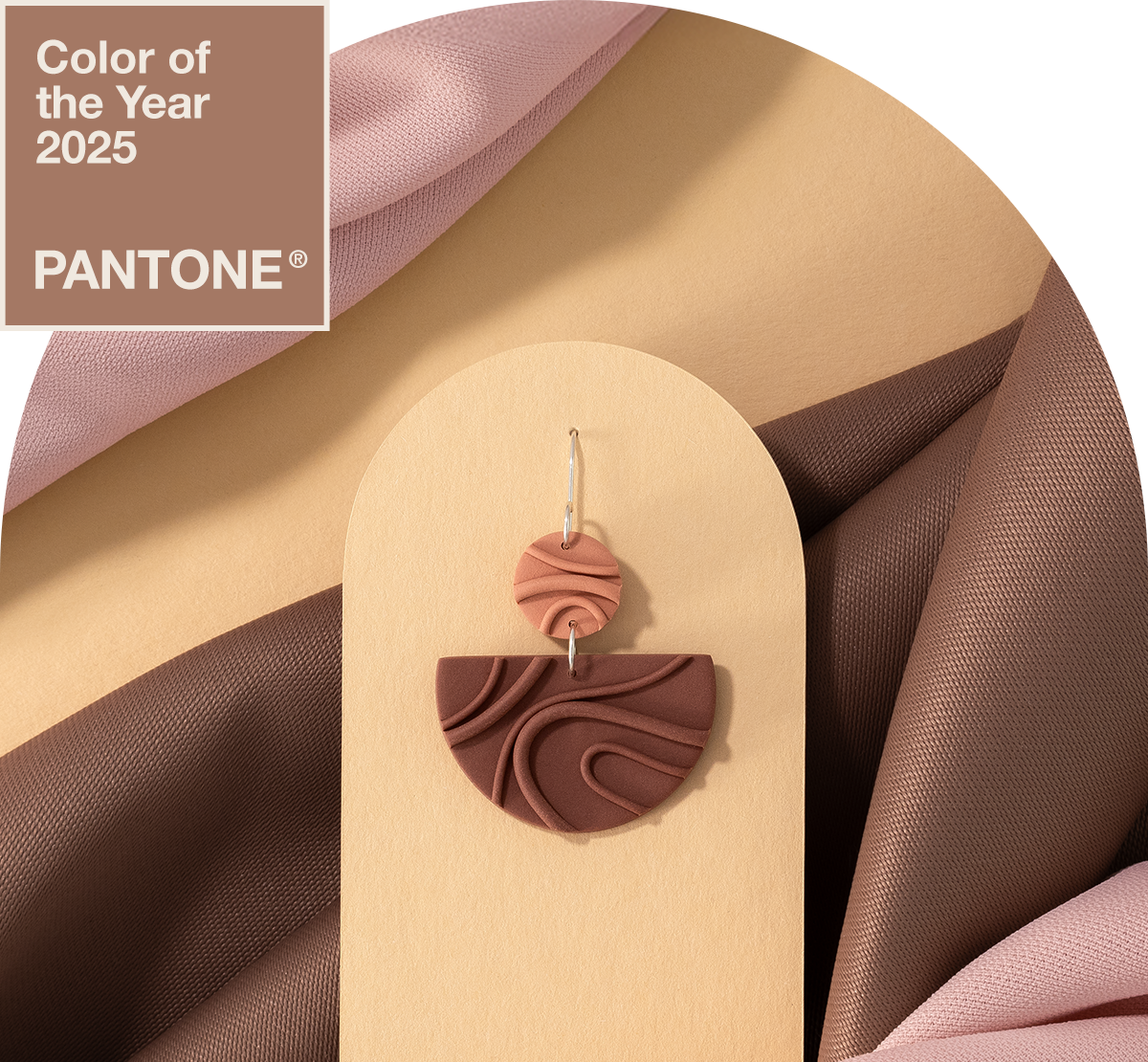 Earring from Mocha Mousse collection on a yellow display with pink and brown fabric, labeled Pantone Color of the Year 2025.