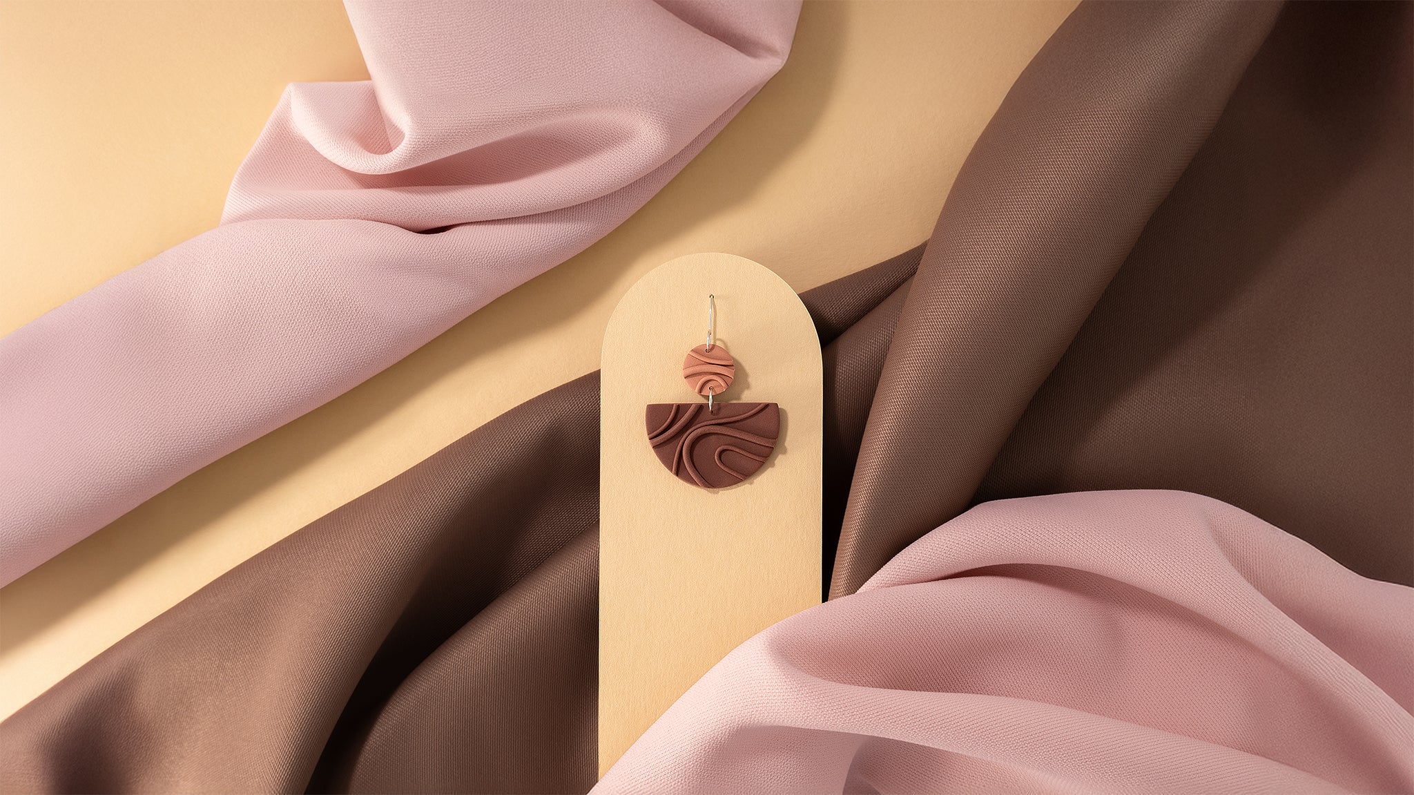 Mocha Mousse N°3 handmade dangle earring with 925 sterling silver findings from Portamira’s Mocha Mousse collection – creamy brown geometric shapes on yellow display with pink and brown fabric.