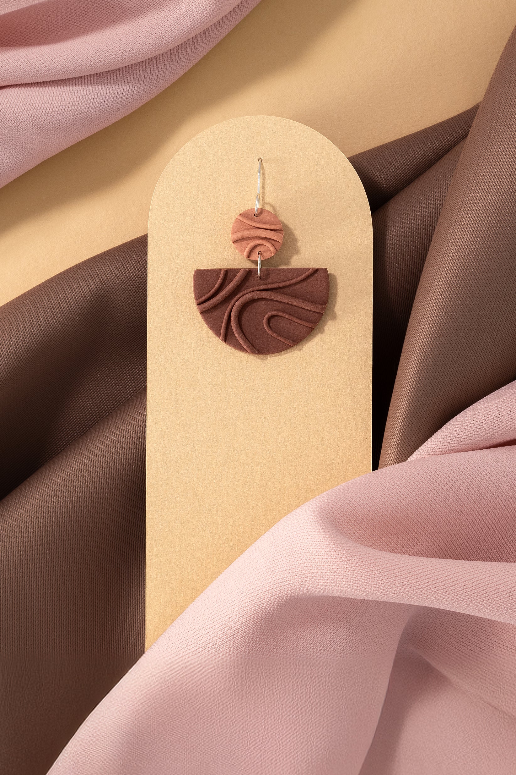 Mocha Mousse N°3 handmade dangle earring with 925 sterling silver findings from Portamira’s Mocha Mousse collection – creamy brown geometric shapes on yellow display with pink and brown fabric.