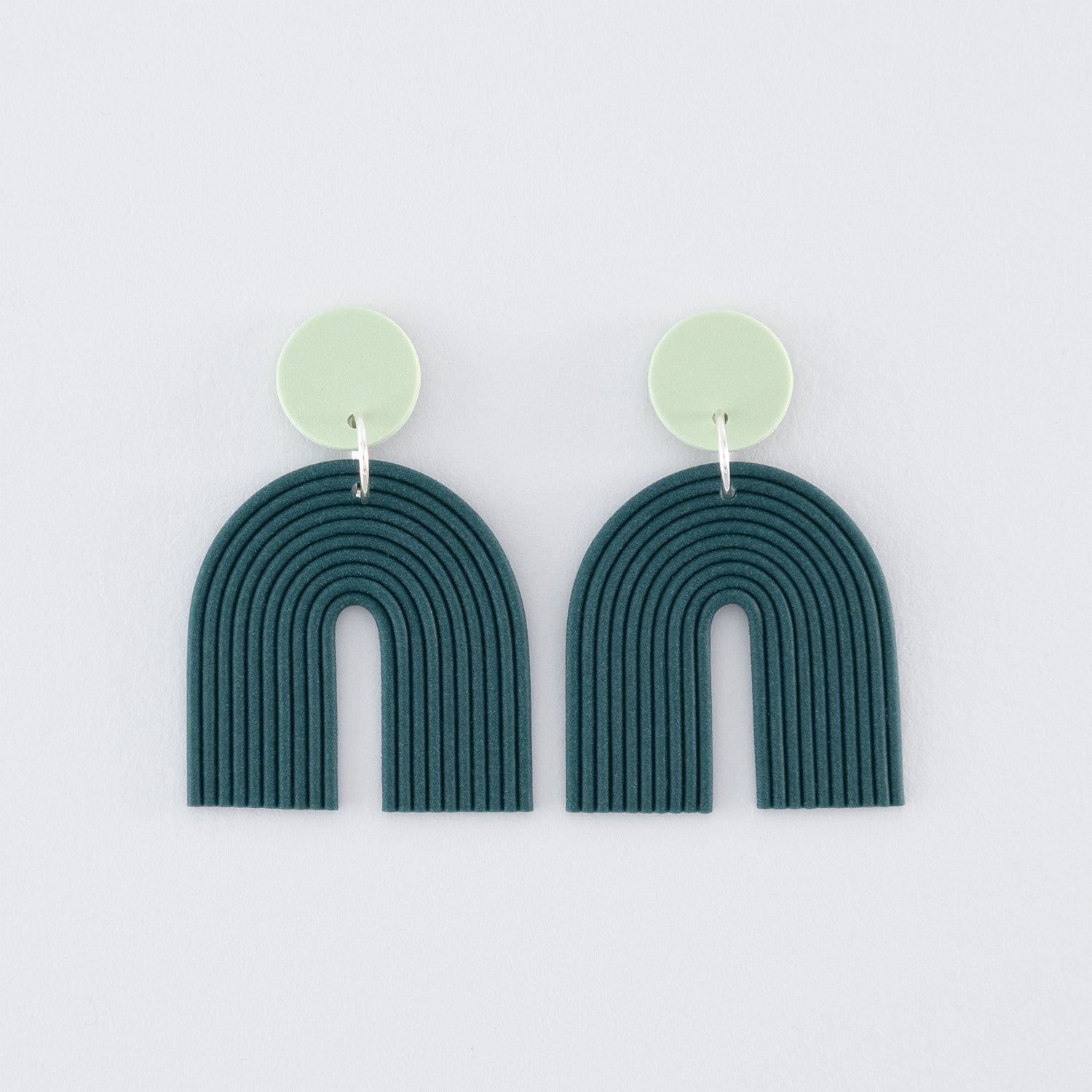 Folium N°2 handmade dangle earrings – delicate, boho, nature-inspired, arch-shaped earrings in smokey teal and pale green with 925 sterling silver findings on a light grey background.