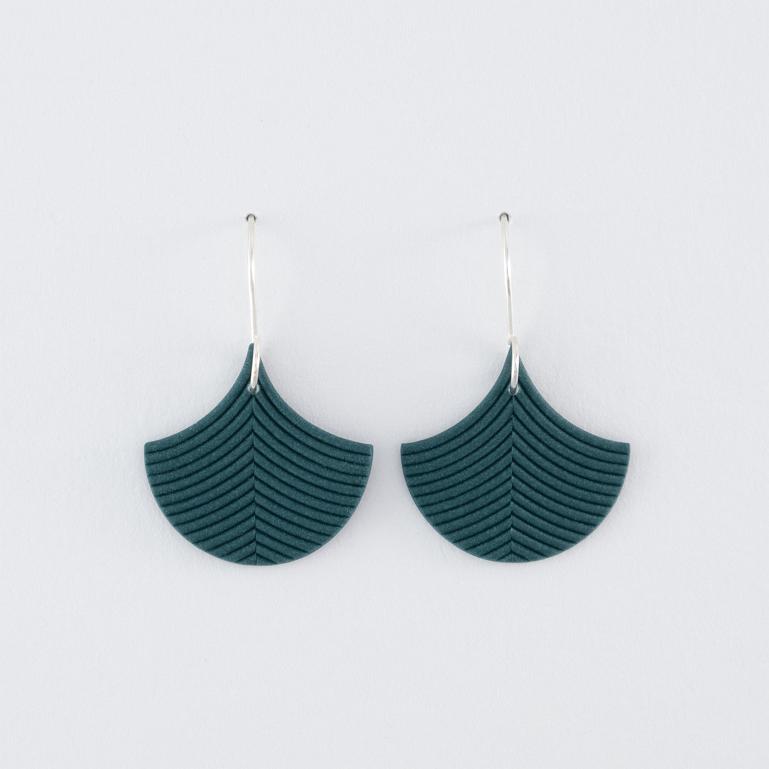 Folium N°3 handmade dangle earrings – delicate, ginkgo leaf-shaped earrings in smokey teal, fitted with 925 sterling silver findings on a light grey background.