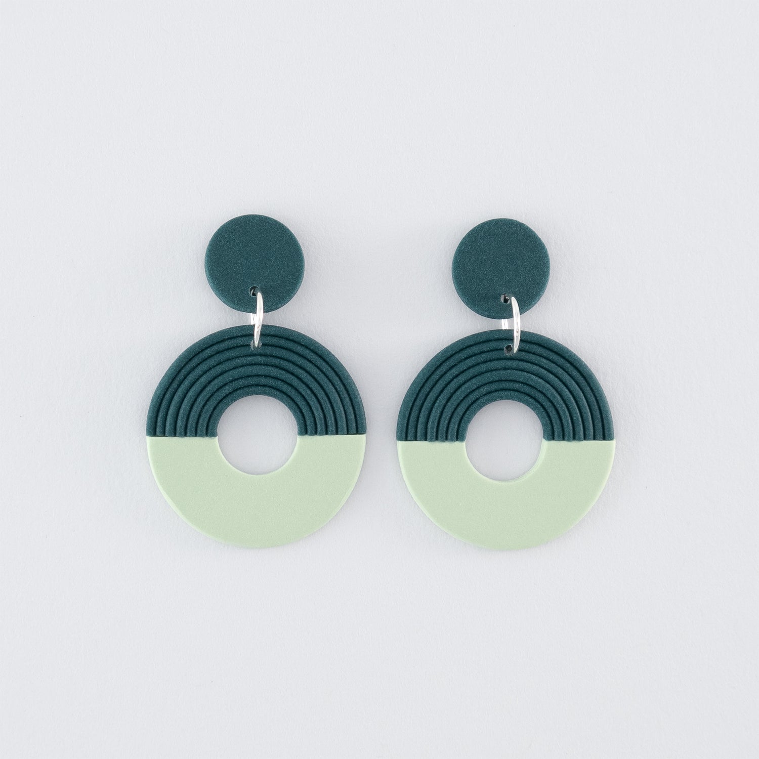 A pair of Folium N°4 handmade dangle earrings – delicate, round, nature-inspired earrings in smokey teal and pale green with 925 sterling silver findings on a light grey background.