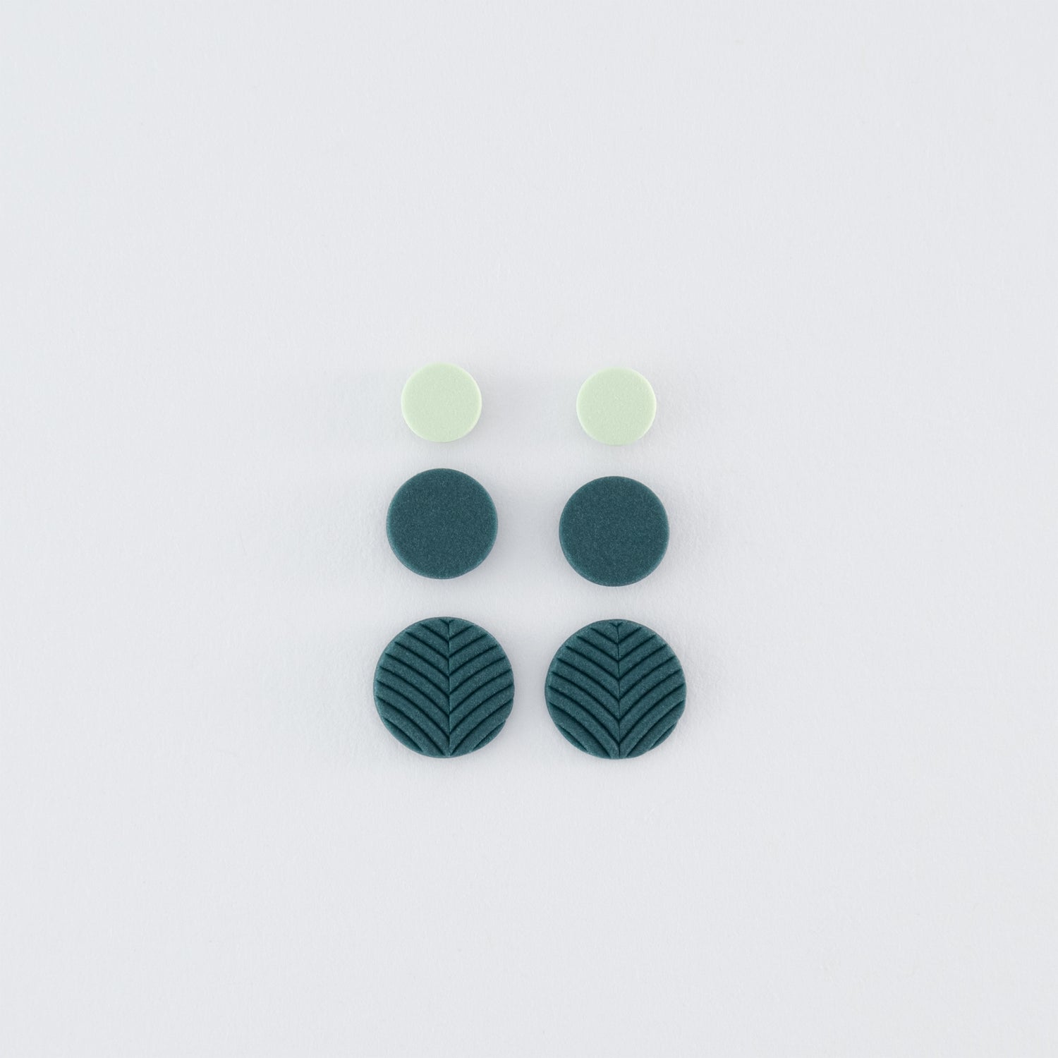 A set (3 pairs) of Folium N°5 handmade studs – delicate, round, nature-inspired earrings in smokey teal and pale green with 925 sterling silver findings on a light grey background.