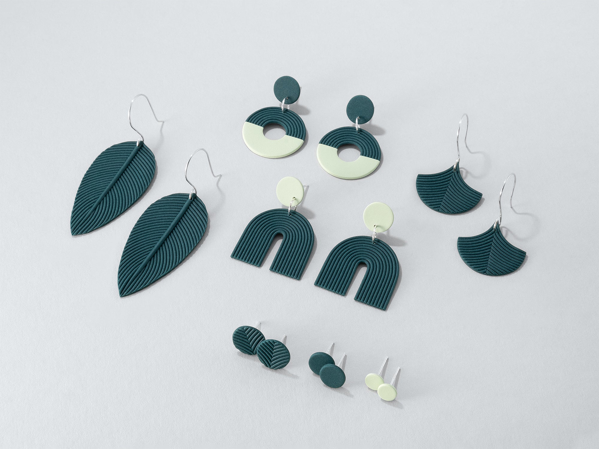 Smokey teal and pale green earrings from the Folium collection – delicate, finely detailed studs and dangling earrings with 925 sterling silver on light grey background. 